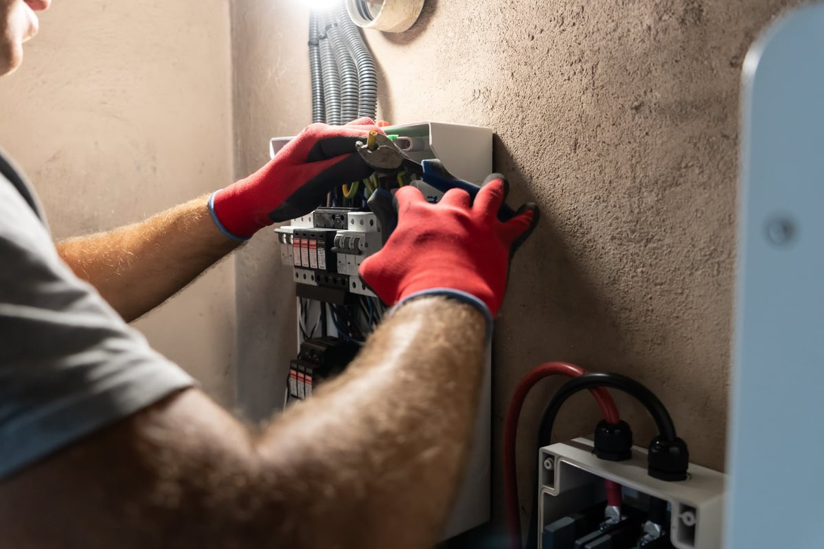 Electrician in gloves working carefully inside an open electrical panel