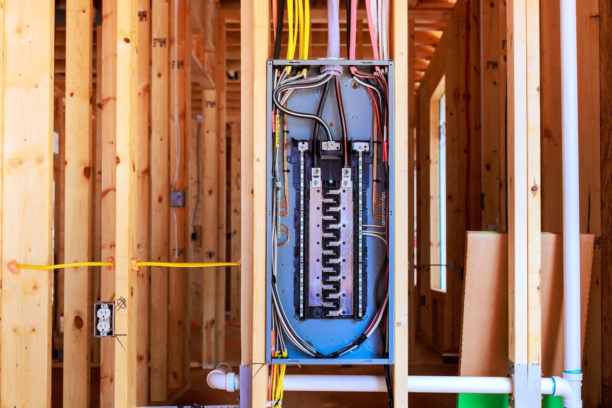 Workers installing an electrical panel in a newly built house with exposed wiring