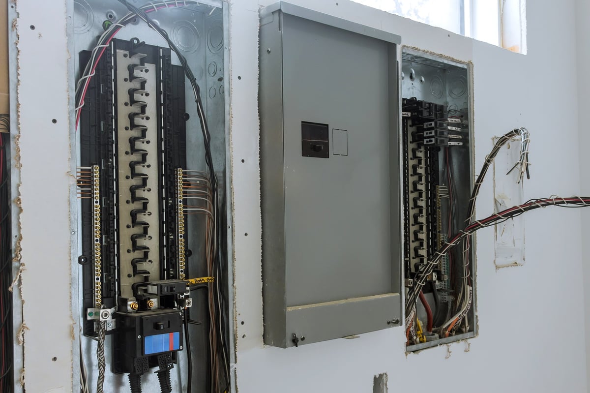 Workers inspecting open electrical panels with exposed wiring during a renovation